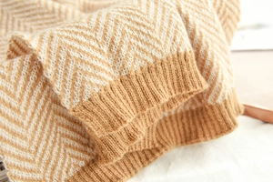 Close-up of beige herringbone knit fabric showing thick texture and ribbed edge