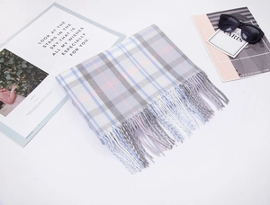 Flat lay of plaid cashmere-like scarf with tassels next to a magazine and sunglasses