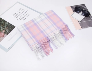 Flat lay of a pastel pink and purple plaid scarf with fringe tassels and fashion accessories