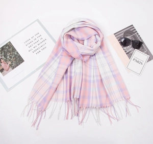 Detail of soft pink and purple plaid scarf with decorative fringe on a white surface