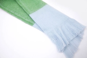 Detail of light blue and green striped knit scarf with soft tassel fringe edges