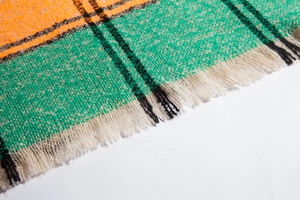 Detailed view of thick knit scarf fabric with orange and green plaid pattern and fringe