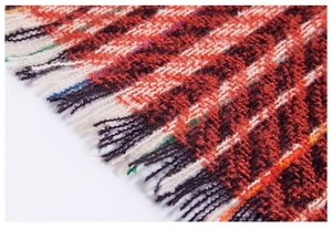 Macro detail of red and white herringbone knit shawl with dense fringe tassel edges