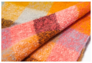 Detailed macro shot of thick colorful plaid knit scarf featuring fuzzy texture fibers