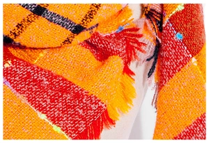 Close-up of thick orange and red plaid scarf fabric with textured weave and fringe detail