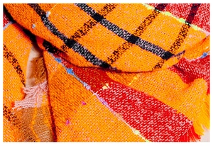 Macro view of thick orange and red plaid scarf featuring soft textured knit and fringe detail
