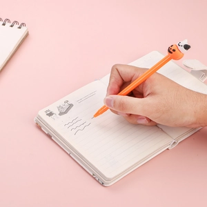 Gros plan d'un stylo gel Halloween écrivant sur un carnet avec figurines citrouille et fantôme