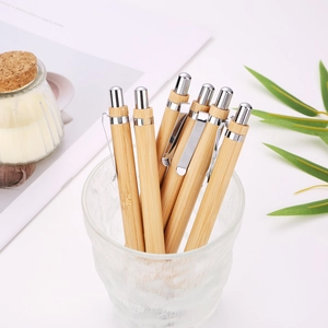 Close-up of bamboo ballpoint pens with silver metal clips in a glass cup on desk