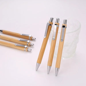 Close-up of bamboo ballpoint pens with silver metal clips in a glass cup on gray background