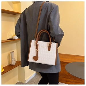 Detail of white quilted tote bag with brown trim and heart charm on a female model