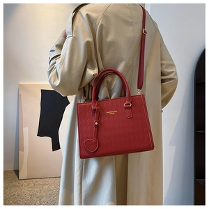 Dark red quilted PU leather handbag with heart pendant shown on beige trench coat