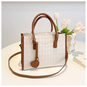 Detail of white quilted tote bag with brown leather handles and heart charm accessory