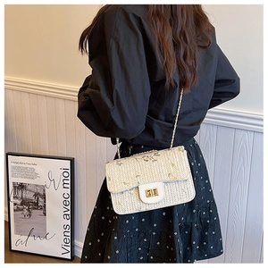 Detailed embroidery of green flowers on a beige woven straw saddle bag with gold chain