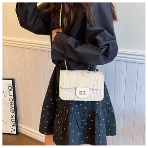 Detail of floral embroidery and gold twist lock on ivory woven straw saddle bag