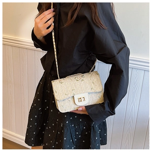 Detail of straw woven crossbody bag with delicate floral embroidery and gold chain strap