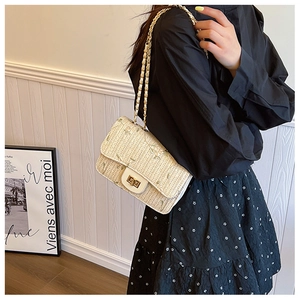 Detail of beige woven straw shoulder bag featuring a light gold twist lock and chain strap