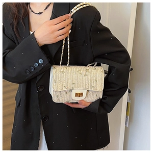 Detail of straw woven saddle bag featuring green embroidery and golden chain strap