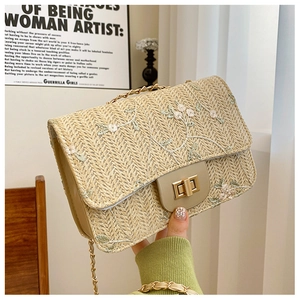 Detail of straw woven bag featuring floral embroidery and a gold twist lock closure