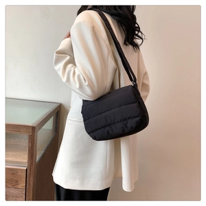 Side view of a black quilted bubble cotton tote bag worn by a model in a minimalist room