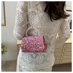 Close-up of pink sequined handbag featuring large pearl handle and gold chain strap