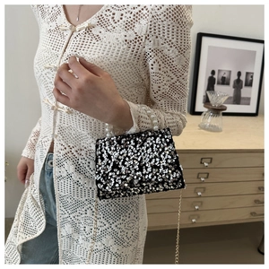Detail of silver sequin handbag with pearl handle and gold chain on model shoulder