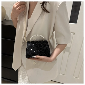 Detail of black sequin handbag with white pearl handle on a model in beige suit