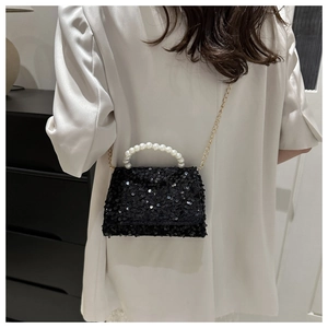 Detail of elegant black sequin handbag with large faux pearl handle and gold chain strap