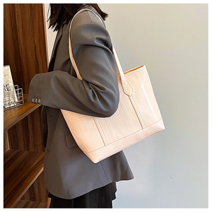 Détail du sac cabas beige à texture crocodile porté par un mannequin en costume