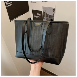 Gros plan d'un sac cabas noir avec texture ondulée, bordure en cuir lisse et logo doré