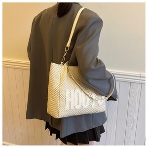 Detail of cream woven tote bag featuring white letter embroidery and leather chain straps