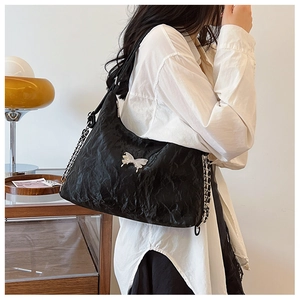 Detail of black tote bag with silver butterfly charm and chain strap on shoulder