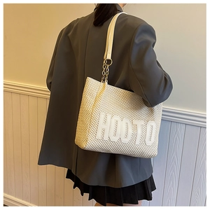 Detailed close-up of beige woven tote bag with HOOTO letter patch and gold metal chain
