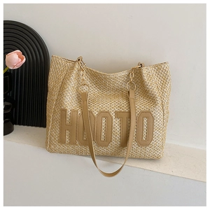 Detail of woven straw tote bag featuring HOOTO logo patch and metal chain strap