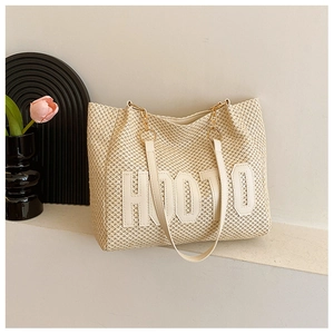 Detail of woven straw tote bag featuring white leather letter patches and gold hardware