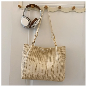 Detail of beige straw tote bag with HOOTO letter patch and gold chain handles