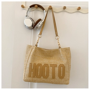 Detail of woven straw tote bag featuring brown leather HOOTO letter patch and strap