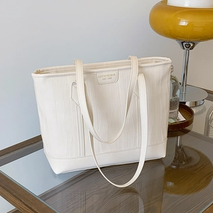 Sac fourre-tout beige minimaliste avec texture ondulée et étiquette sur table en verre