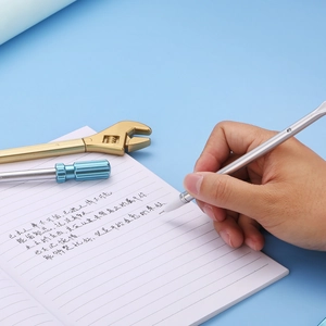 Close-up of a silver wrench-shaped gel pen writing on paper with tool accessories