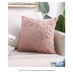Pink plush throw pillow with gold feather patterns on a sofa with green plants