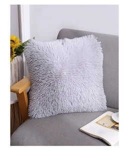 Close-up of a soft grey long-pile faux fur cushion on a sofa with a magazine and flowers
