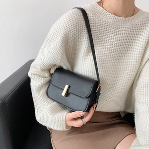 Classic black saddle shoulder bag with gold metal buckle shown on model in modern style
