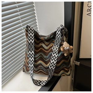 Detail of woven tote bag with wavy patterns, wide geometric strap and plush monster charm
