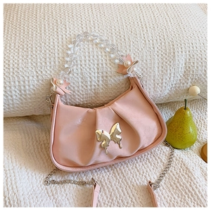 Sac bandoulière plissé rose avec breloque papillon et anse perlée sur tissu blanc