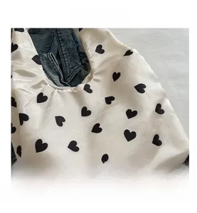 Close-up of white satin tote bag featuring a black heart pattern and silky texture