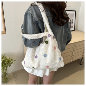 Detail of white knitted tote bag with colorful flower embroidery shown on shoulder