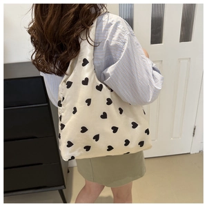 Minimalist off-white nylon tote bag with black heart prints worn on shoulder