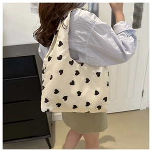 Detail showing beige tote bag with black heart prints worn on the shoulder in daily life