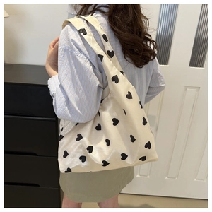 Chic cream satin tote bag with black heart prints worn by model in casual style