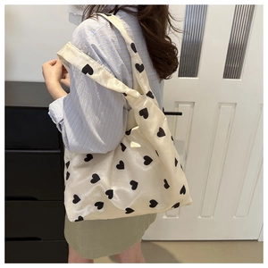 Detailed side view of beige nylon tote bag with black heart prints on shoulder