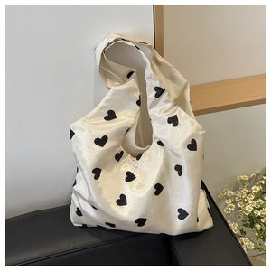 Cream nylon hobo bag with black heart prints on a black leather sofa background